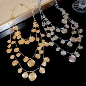 Detail of layered gold and silver necklaces with brushed metal discs on a black surface