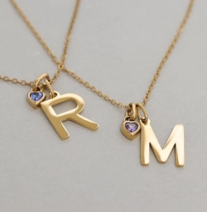 Macro detail of gold-plated necklaces with alphabet R M and purple zircon heart pendants