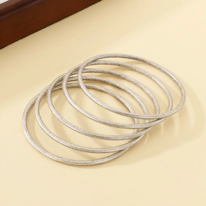 Close-up of six stacked silver stainless steel bangles with brushed metallic texture