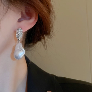 Close-up of irregular silver drop earrings with baroque pearl on a female model