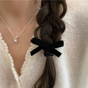 Detail view of a black velvet bow hair tie worn on a braided hairstyle for a vintage look