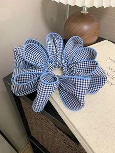 Close-up of blue gingham fabric scrunchie with lace edge on a beige book