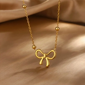 Golden titanium steel bow pendant necklace with beaded chain on elegant fabric background
