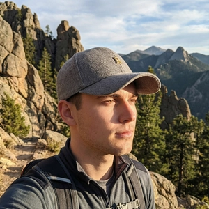 Grey herringbone baseball cap with gold metal R logo worn by a man in scenic mountains