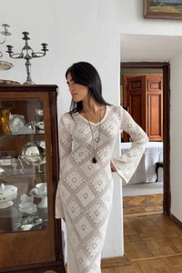 Dettaglio di un abito lungo in maglia crema con texture geometriche traforate e maniche lunghe