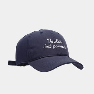 Close-up of navy blue cotton baseball cap with white Vouloir c'est pouvoir embroidery