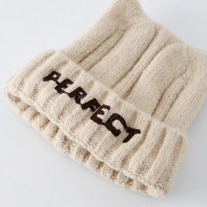 Detailed close-up of cream knit baby hat showing thick texture and PERFECT embroidery