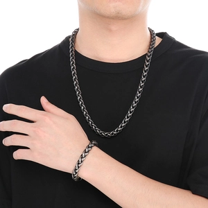 Détail d'un ensemble collier et bracelet en maille tressée noire porté par un homme