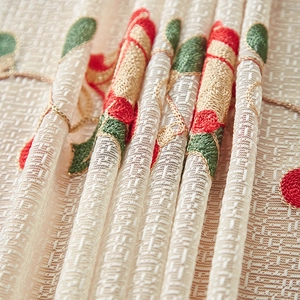 Detailed close-up of red floral embroidery on beige lace fabric with grid mesh texture