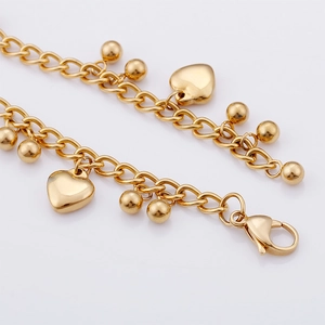 Detail of gold titanium steel bracelet featuring heart and bead charms with lobster clasp