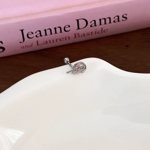 Macro detail of lollipop-shaped silver earring with pink zircon on white porcelain plate