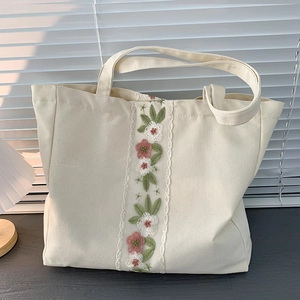 Dettaglio di ricamo floreale su borsa tote in tela color crema su piano in legno