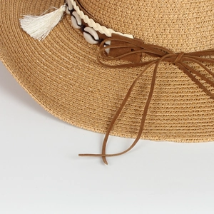 Macro shot of straw sun hat featuring seashell band, white tassel and brown suede ties