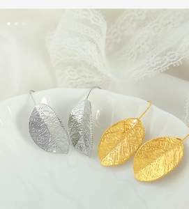 Detailed view of gold and silver hollow leaf earrings on a white ceramic tray