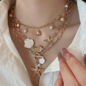 Detail of bohemian layered necklace with golden starfish, shell charms and small pearls