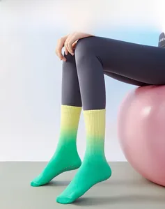Green and yellow gradient mid-tube yoga socks with anti-slip grip dots on a yoga ball