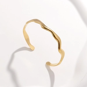 Detail eines goldenen wellenförmigen Armreifs mit minimalistischem Lava-Design