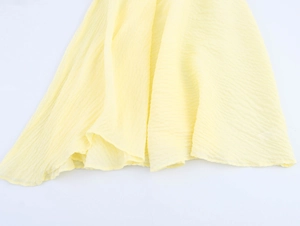 Detail showing the light yellow textured fabric and pleated hemline of this summer dress