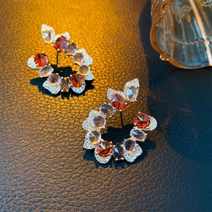 Detailed view of golden leaf earrings with red and clear crystals on dark leather