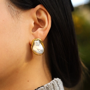 Close-up of elegant baroque pearl earrings with gold frame worn on a model's ear
