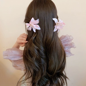 Detail of pink fabric hibiscus flower clips worn on wavy brown hair for a romantic look