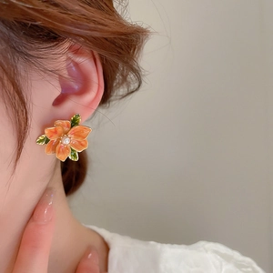 Close-up of orange floral earring with pearl and green leaf on a model ear