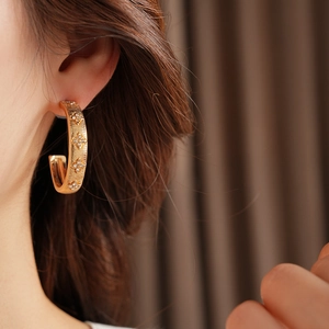 Close-up of gold C-shaped hoop earrings with diamond flower texture on model