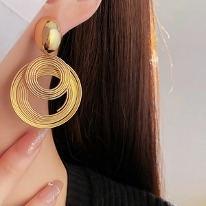 Close-up of large golden spiral hoop earrings worn by a model in a minimalist style