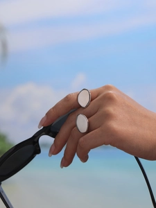 Silver oval geometric ring on hand held in front of a sunny beach landscape