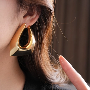 Close-up of geometric gold-plated earrings with smooth metal finish on a model's ear