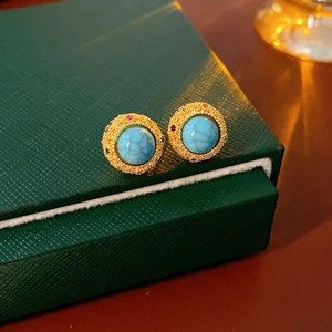 Detail of turquoise stud earrings with 18k gold-plated filigree on a jewelry box