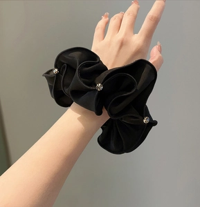 Detailed view of a black satin scrunchie with sparkling rhinestones on model's wrist