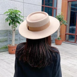 Back view of a beige flat top wool fedora hat with a brown ribbon band on a model