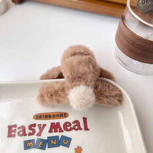 Close-up of a plush coffee brown hair claw clip with soft white pom-poms on a tray