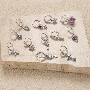 Set of 11 stainless steel nose rings with colorful zircon charms on a stone surface