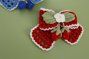 Detailed macro view of handmade crochet strawberry hair clip with red and white yarn bow