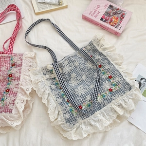 Detail of floral embroidery and white lace ruffles on plaid canvas tote bags