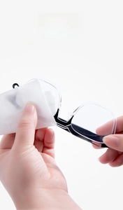 Close-up of hands using a disposable anti-fog wipe to clean black full-rim eyeglasses