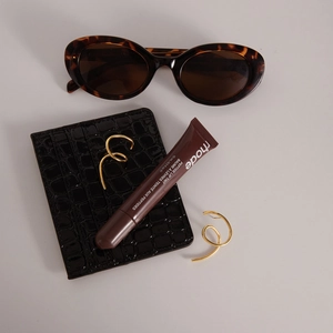Flat lay of gold spiral earrings with tortoiseshell sunglasses and peptide lip tint