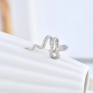 Macro shot of silver snake ear cuff with textured scales on white ceramic surface