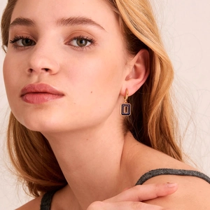 Close-up of golden hoop earrings with deep blue rectangular pendant on female model