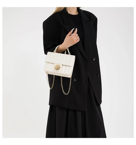 Close-up of white leather crossbody bag featuring gold metal buckle and chain strap on model