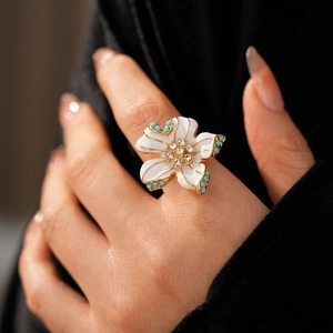 Gros plan d'une bague fleur en émail blanc avec bords dorés et cristaux sur le doigt