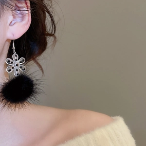 Detail of plush black pom-pom and acrylic flower earrings on model with knitwear