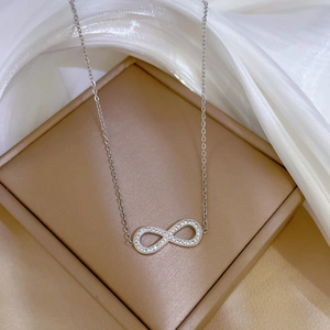 Macro shot of silver infinity pendant with clear zircons on delicate chain over silk