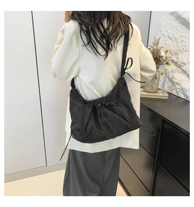 Detail of black pleated canvas tote bag with adjustable drawstring and wide strap on model
