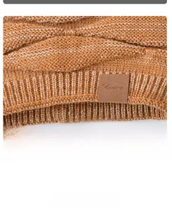 Detail der groben Zopfstrick-Textur und des braunen Sport-Leder-Logos an der Strickmütze