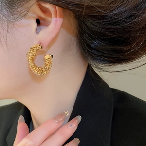 Close-up of a gold-plated twisted C-shaped earring worn by a model in a side view