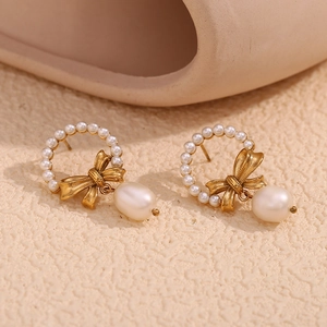 Close-up of vintage gold bow earrings with baroque pearl drop on elegant beige backdrop