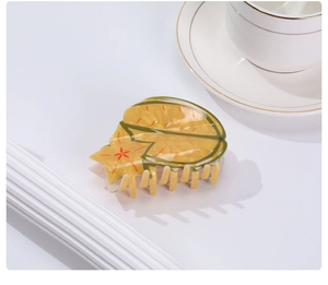 Macro view of a yellow star-patterned hair claw clip on a minimalist white desk with a tea cup